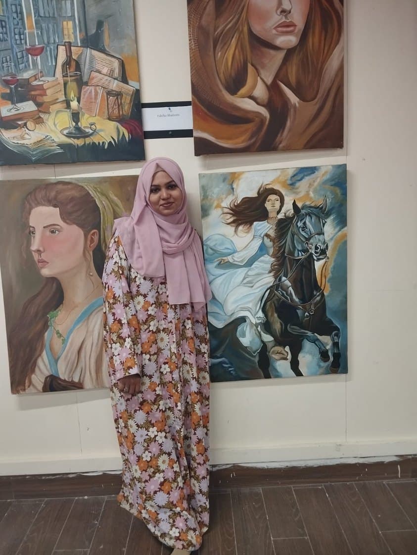 Fabiha Shaheen standing before a wall of her paintings in a gallery.